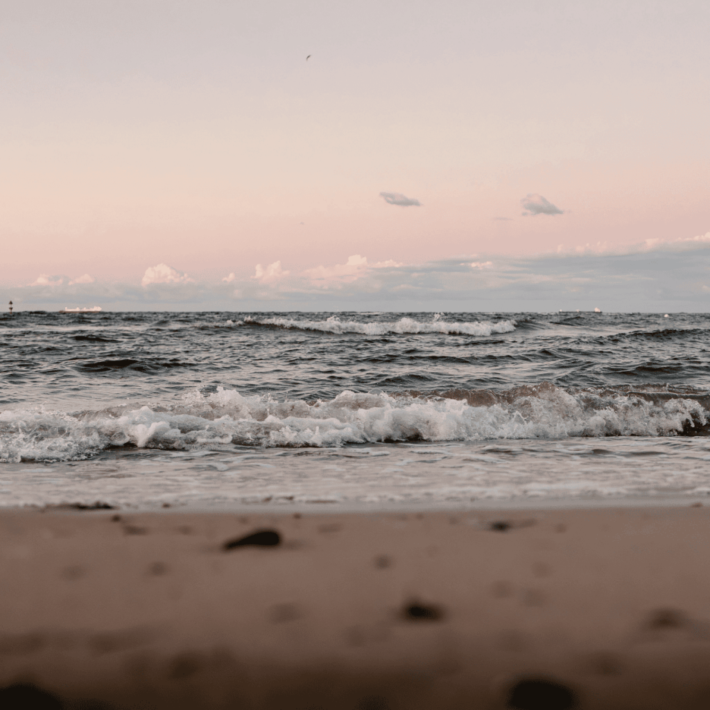 Blick aufs Meer mit leichten Wellen bei Sonnenuntergang am Sandstrand.
